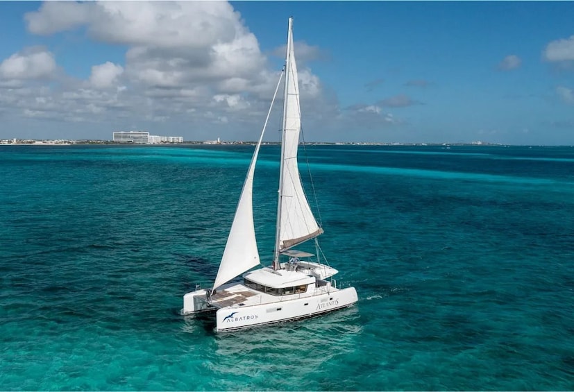 Eine Segelyacht namens 'Atlantis' auf türkisfarbenem Wasser, bewölkter Himmel und Gebäude in der Ferne. 1