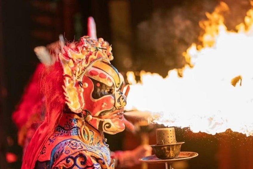 A person in traditional attire with a mask and red hair, holding a ritual object. 2