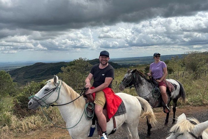 Two people riding horses on a trail with a mountainous landscape in the background. 2