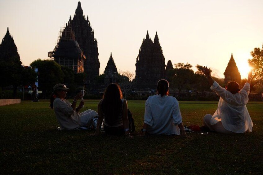 People sitting on grass with a temple in the background during sunset. 4