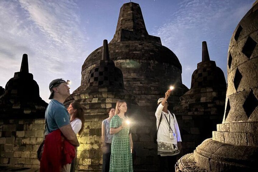 Des touristes observent d'anciennes constructions en pierre sous un ciel dégagé. 1