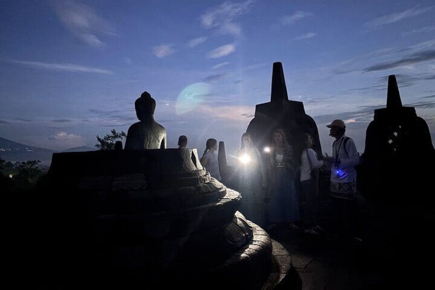 Une statue de Bouddha et un stoupa au crépuscule, avec des visiteurs alentour. 3