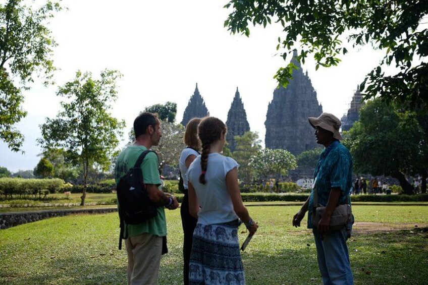 A group of people standing on grass, looking at a temple with tall spires in the background. 2