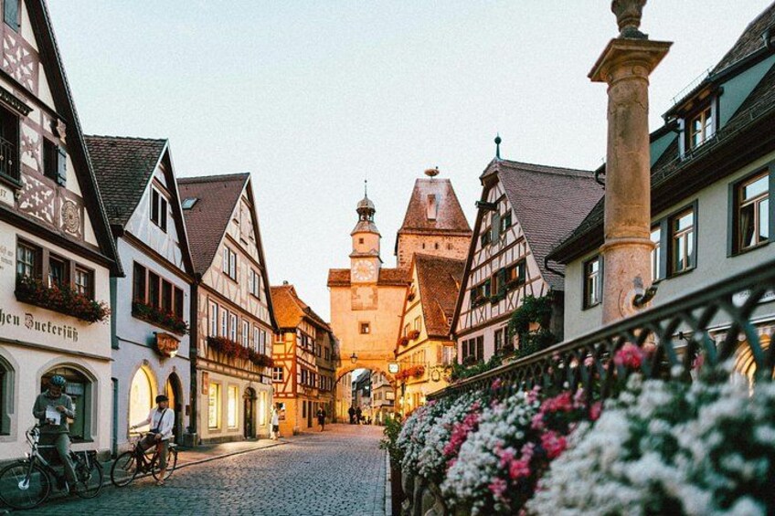 A cobblestone street lined with traditional half-timbered houses, a prominent tower, and a cyclist. 5