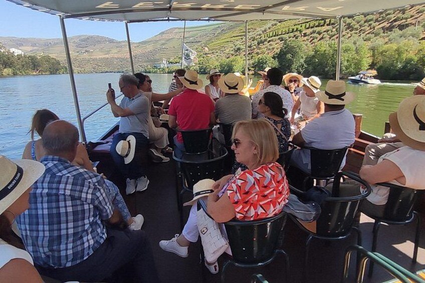 A group of people on a boat, some wearing hats, with a river and hills in the background. 4