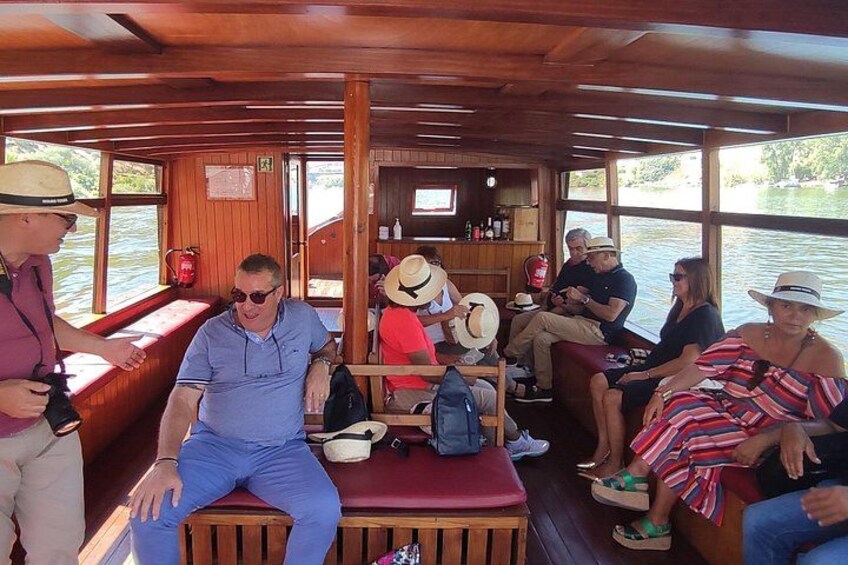 A wooden boat interior with people seated, a bar area, and a view of the water outside. 5