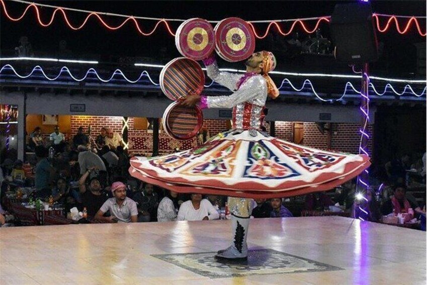 A performer in a colorful, patterned dress balancing on a spinning platform with large circular objects. 3