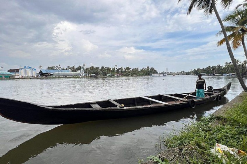 A traditional boat on calm water, a person standing at the stern, and a shoreline with buildings and palm trees in the background. 5