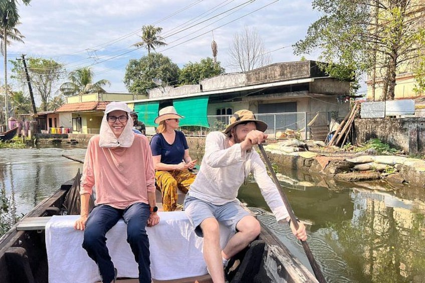 Three people on a boat in a river, surrounded by buildings and trees. 1