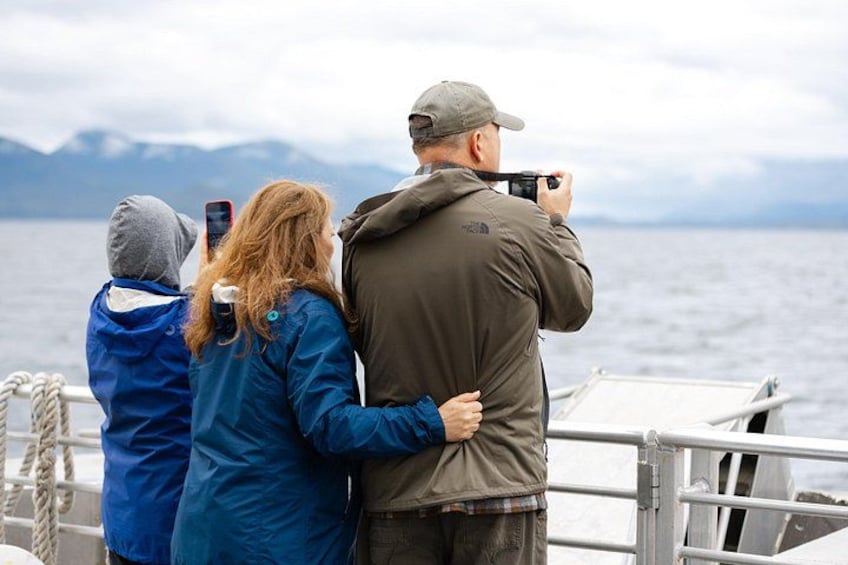Drei Personen in einem Boot, eine macht ein Foto, eine andere hält ein Handy, und eine dritte steht in der Nähe. 2