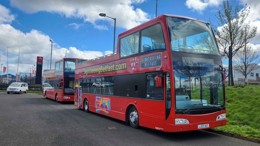 A red double-decker bus with the text "Sightseeing Belfast.com" on its side, parked on a road with a clear sky and some clouds in the background. 4