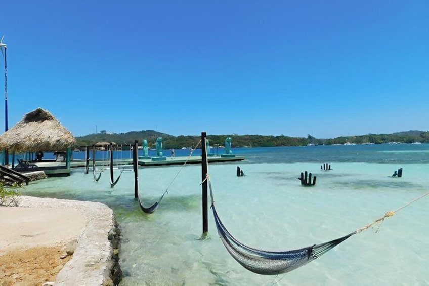 A beach with clear turquoise water, a thatched-roof hut, and a hammock. 2