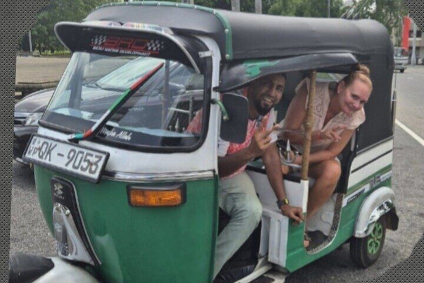A green and white auto-rickshaw with two passengers, one man and one woman, on a road. 1