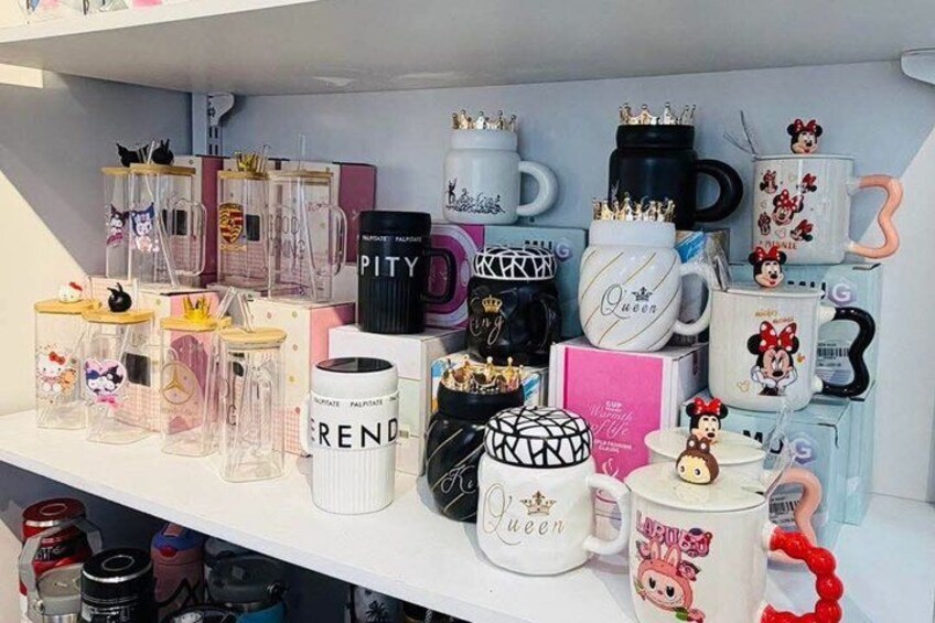 A shelf with various mugs and containers, some with designs and text, others with handles. 1
