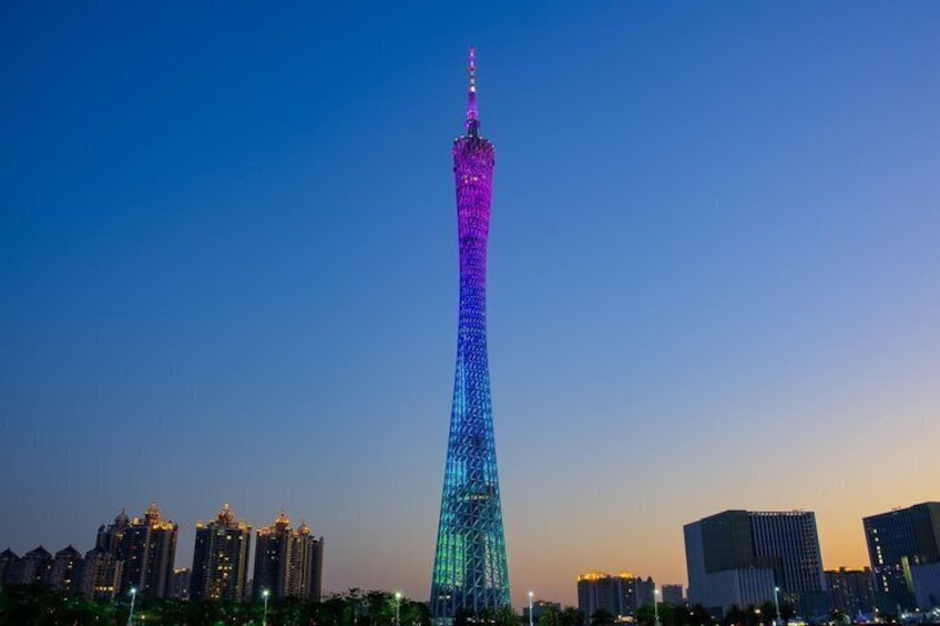 A tall tower with a spire, illuminated in blue and purple lights, surrounded by city buildings. 4