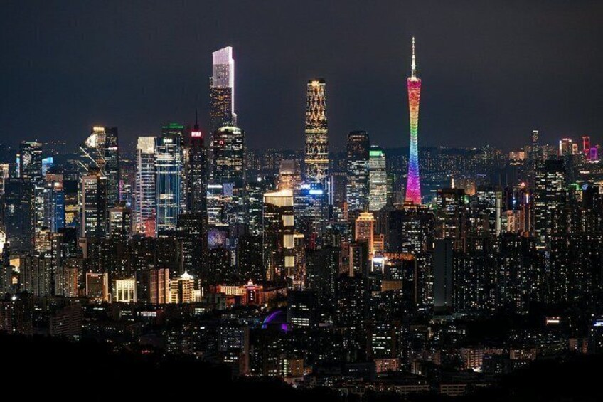 A city skyline at night with illuminated buildings and a prominent tower with a rainbow light display. 2