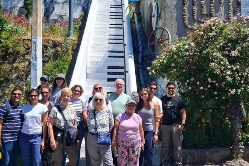 A group of people standing in front of a large piano-like structure with a staircase leading up to it. 3
