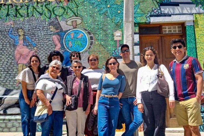 A group of people standing in front of a colorful mural with a door and a wall with a circular emblem. 4