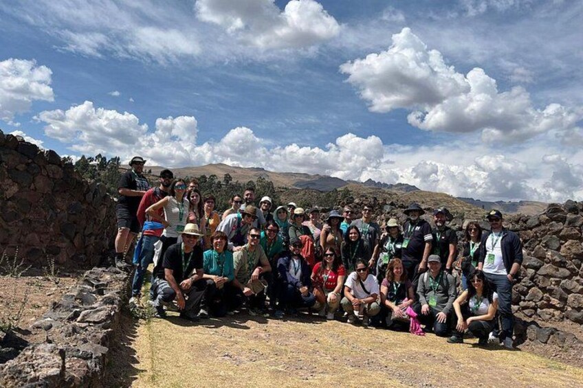 Un groupe de personnes s’est rassemblé à l’extérieur, peut-être lors d’une randonnée ou d’une excursion, avec un mur de pierre et un paysage montagneux en arrière-plan. 4