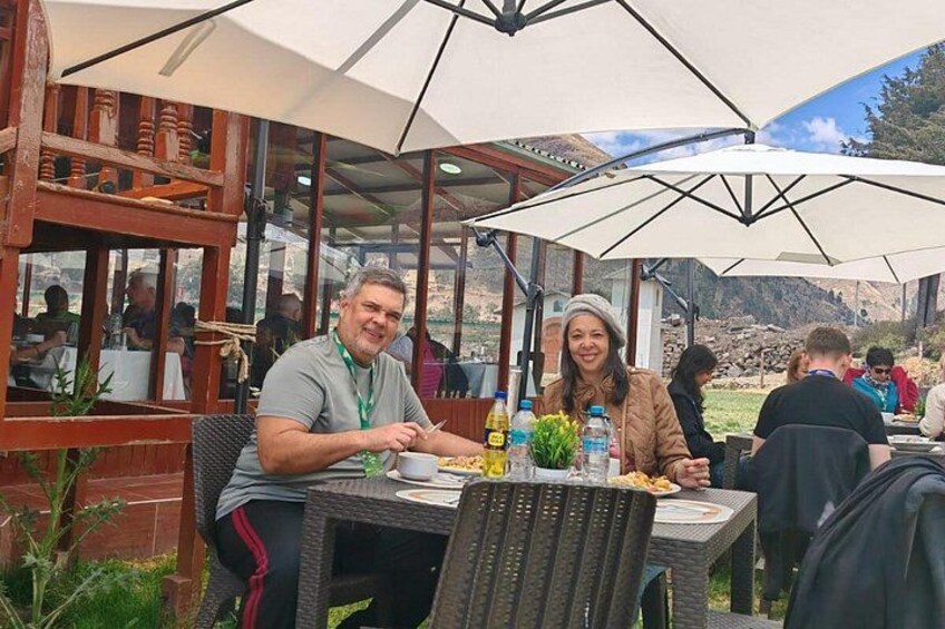 Deux personnes dînent dans un restaurant en plein air, sous des parasols, avec une chaîne de montagnes en arrière-plan. 2