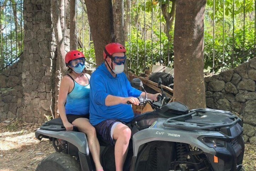 Two people on a quad bike in a wooded area with stone walls. 5