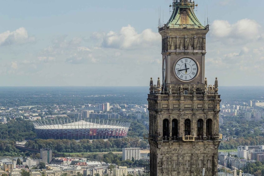 A clock tower with a large clock face, surrounded by a cityscape and a stadium in the background. 5