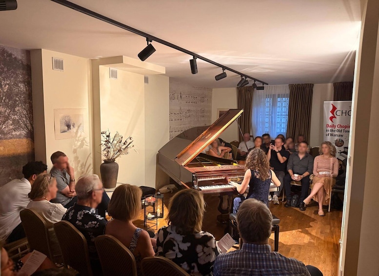 A group of people seated in a room with a grand piano. 2