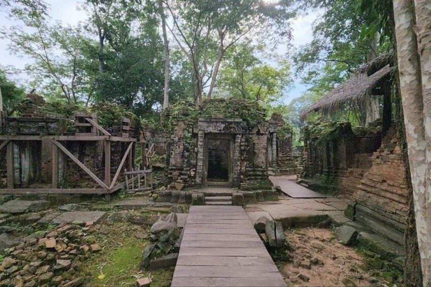 A temple complex with stone structures, a wooden pathway, and surrounding trees. 4