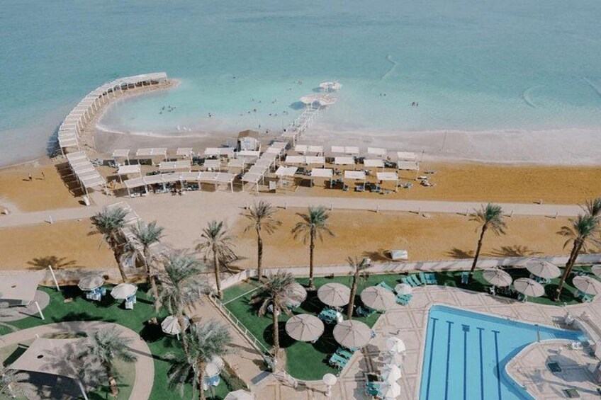 A beach resort with a pool, palm trees, and a curved walkway along the shore. 1