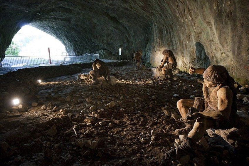 A cave with people sitting on the ground, a flashlight illuminating the area, and a fence visible outside. 2