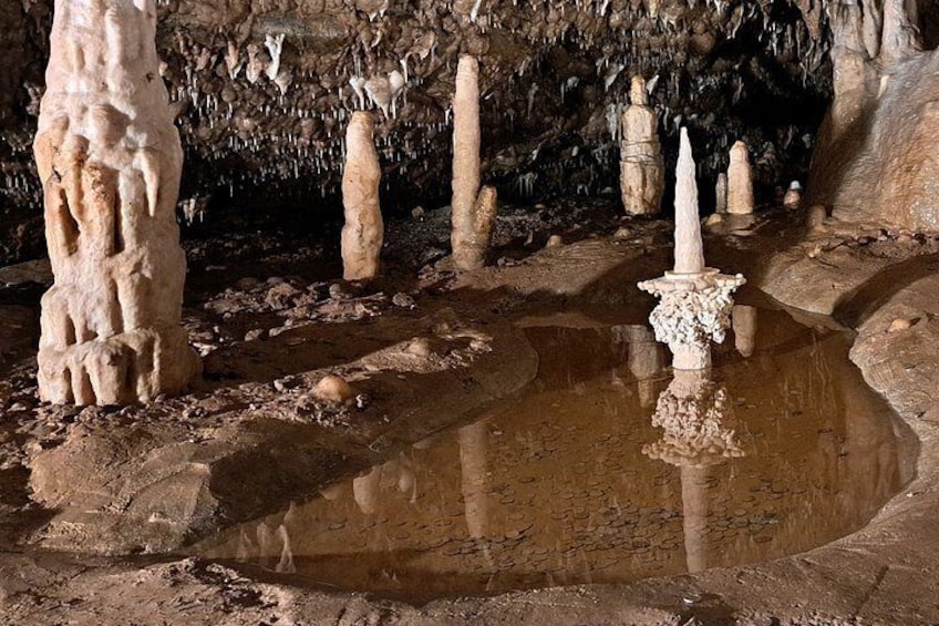 A cave with stalactites, stalagmites, and a central water feature. 1