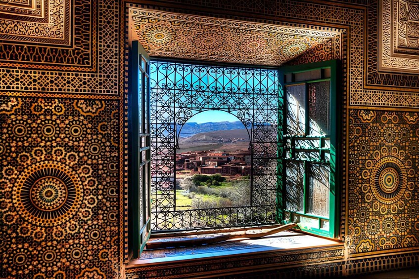 A window with intricate geometric patterns and a view of a town with buildings and mountains in the distance. 2