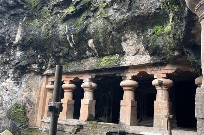 A cave temple entrance with carved pillars and a doorway. 5