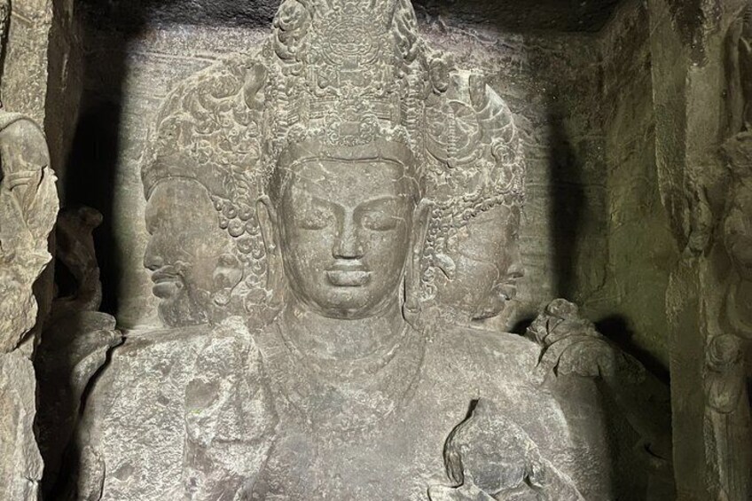 A stone sculpture of a seated figure with elaborate headdress and multiple smaller figures around it. 2