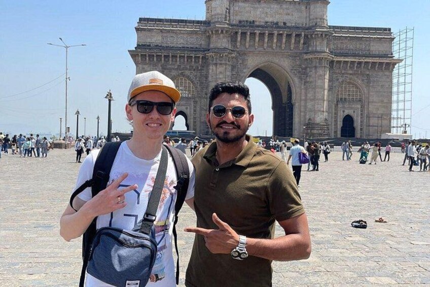 Two people standing in front of a large historical archway with tourists in the background. 2