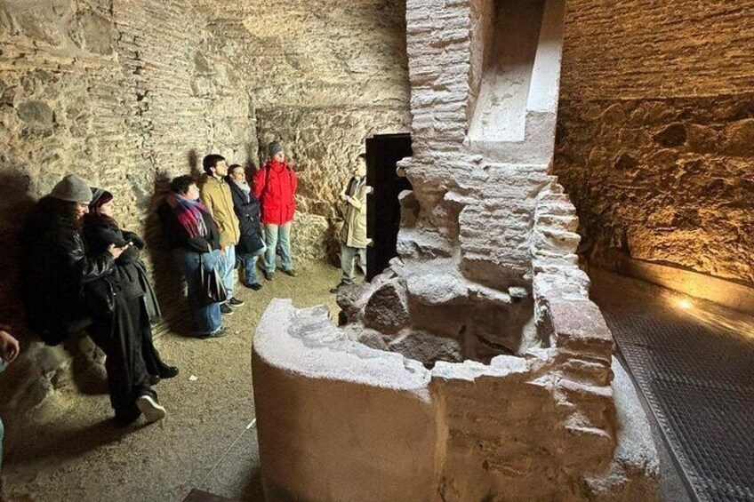 Un groupe de personnes observe des ruines anciennes, avec des murs de pierre et une structure en pierre au premier plan. 1