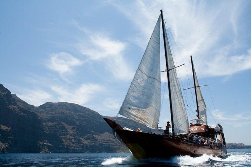 Un velero con dos mástiles navegando sobre aguas tranquilas, con montañas al fondo. 3