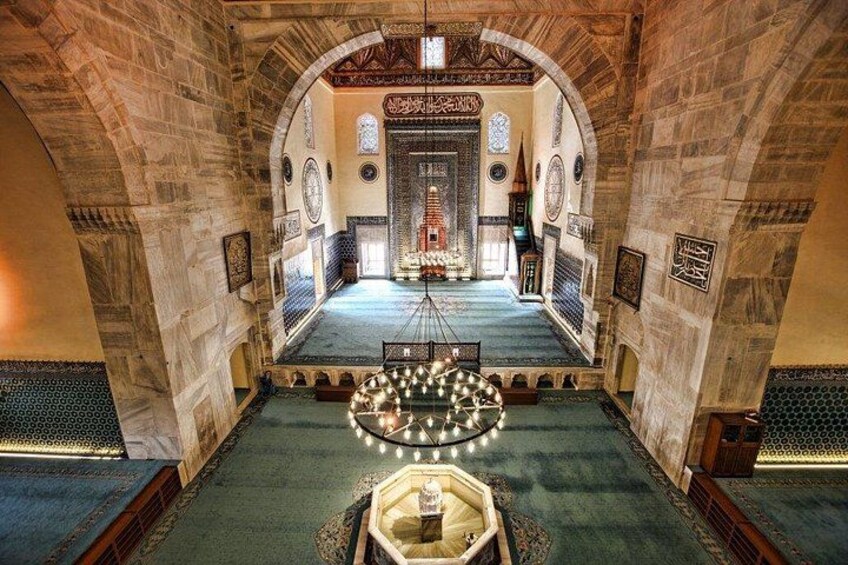 An interior with a central aisle, arched ceilings, patterned walls, and a chandelier. 4