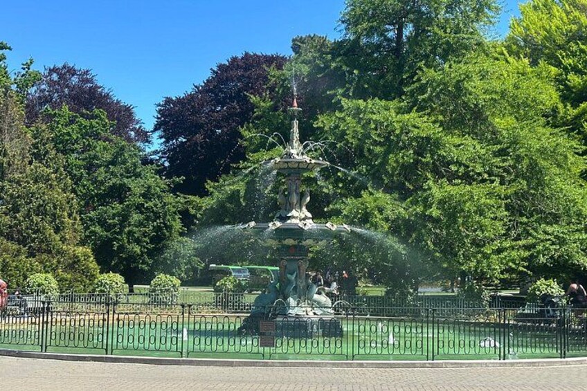 A fountain with water jets in a park with trees and a fence. 3