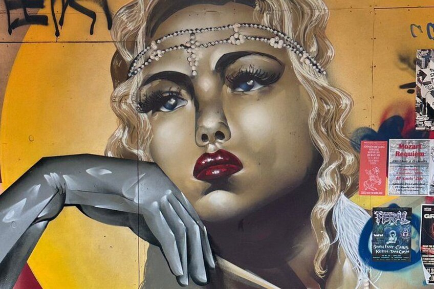 A mural with a woman's face, a metallic hand, and various posters. 2