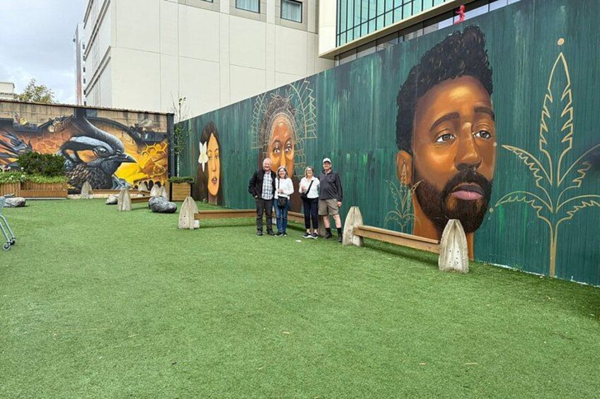 A mural on a building, a grassy area, and a few people standing. 5