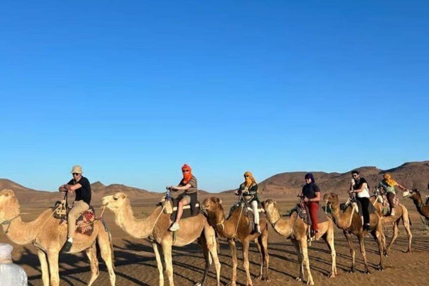 A group of people riding camels in a desert landscape. 1