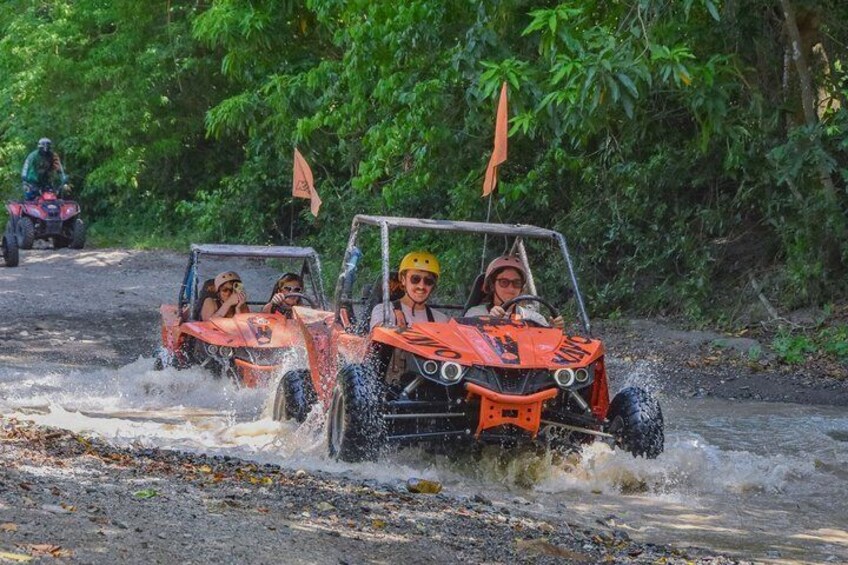 Two orange off-road vehicles driving through a shallow water crossing. 1