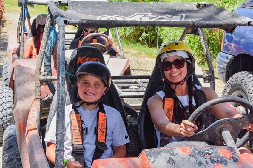 Two people in a vehicle with a steering wheel, wearing safety helmets and harnesses. 3