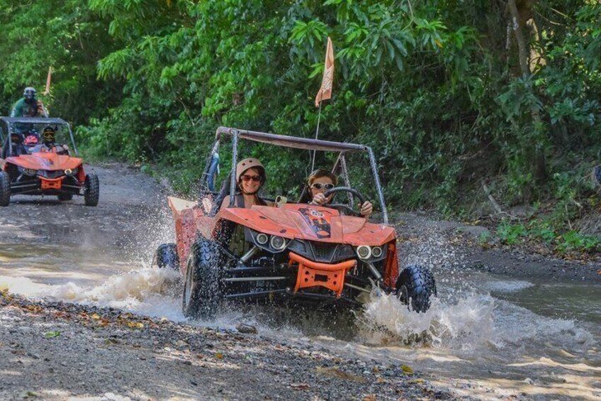 A red off-road vehicle driving through a shallow water crossing. 5