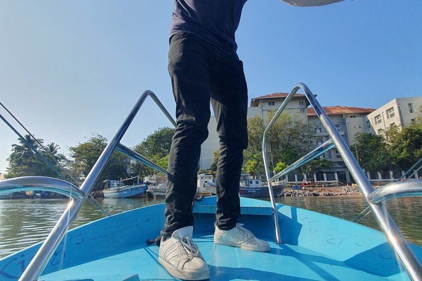 A person standing on a boat with metal railings, water, and buildings in the background. 2