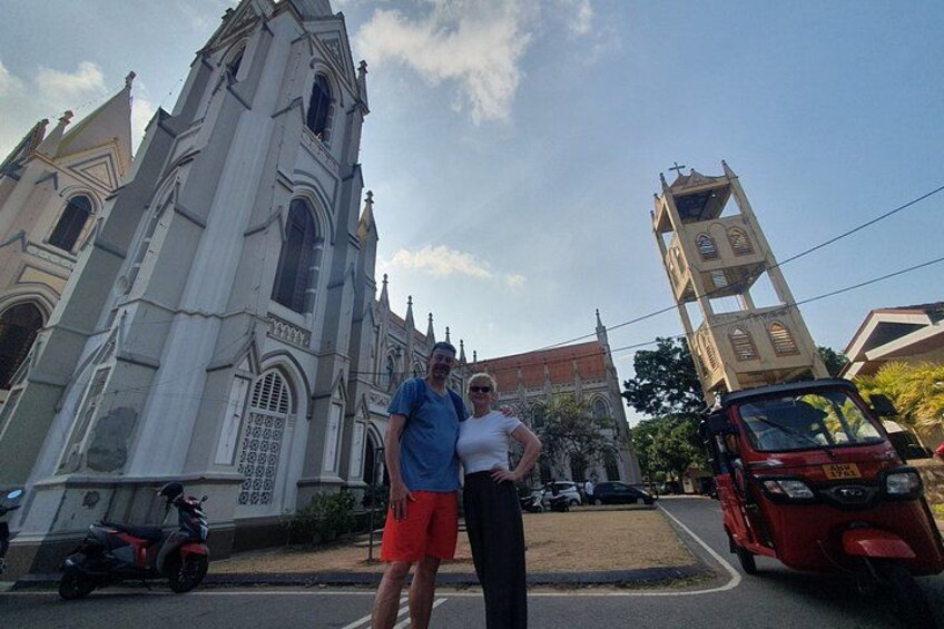 A church with a tall bell tower, a person in red shorts, and a red vehicle parked nearby. 4