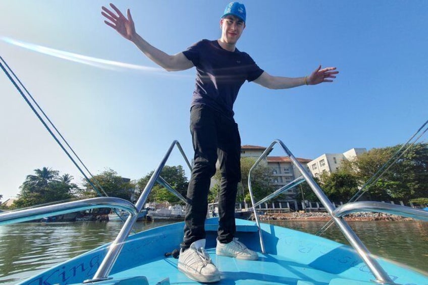 A person standing on a boat with metal railings, water, and buildings in the background. 1