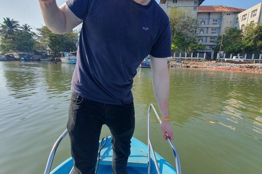 A person standing on a boat with a metal ladder, water in the background, and buildings on the shore. 3
