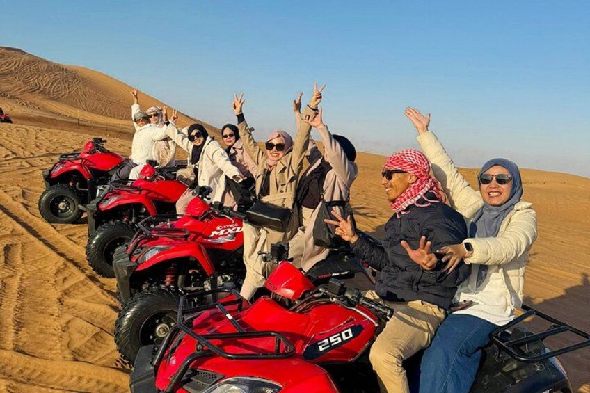 A group of people on red off-road vehicles in a desert with sand dunes. 1